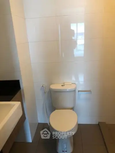 Modern bathroom with sleek fixtures and neutral tiles, featuring a toilet and sink.