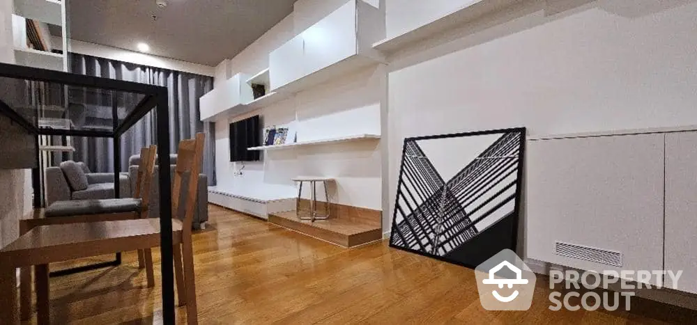 Spacious modern living room with polished hardwood floors, white walls, and contemporary furnishings, leading to an open-plan kitchen area.