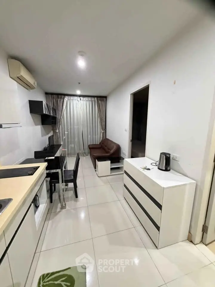 Modern apartment with open kitchen and cozy living area, featuring sleek furniture and tiled flooring.