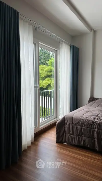 Cozy bedroom with large window and elegant curtains overlooking lush greenery.