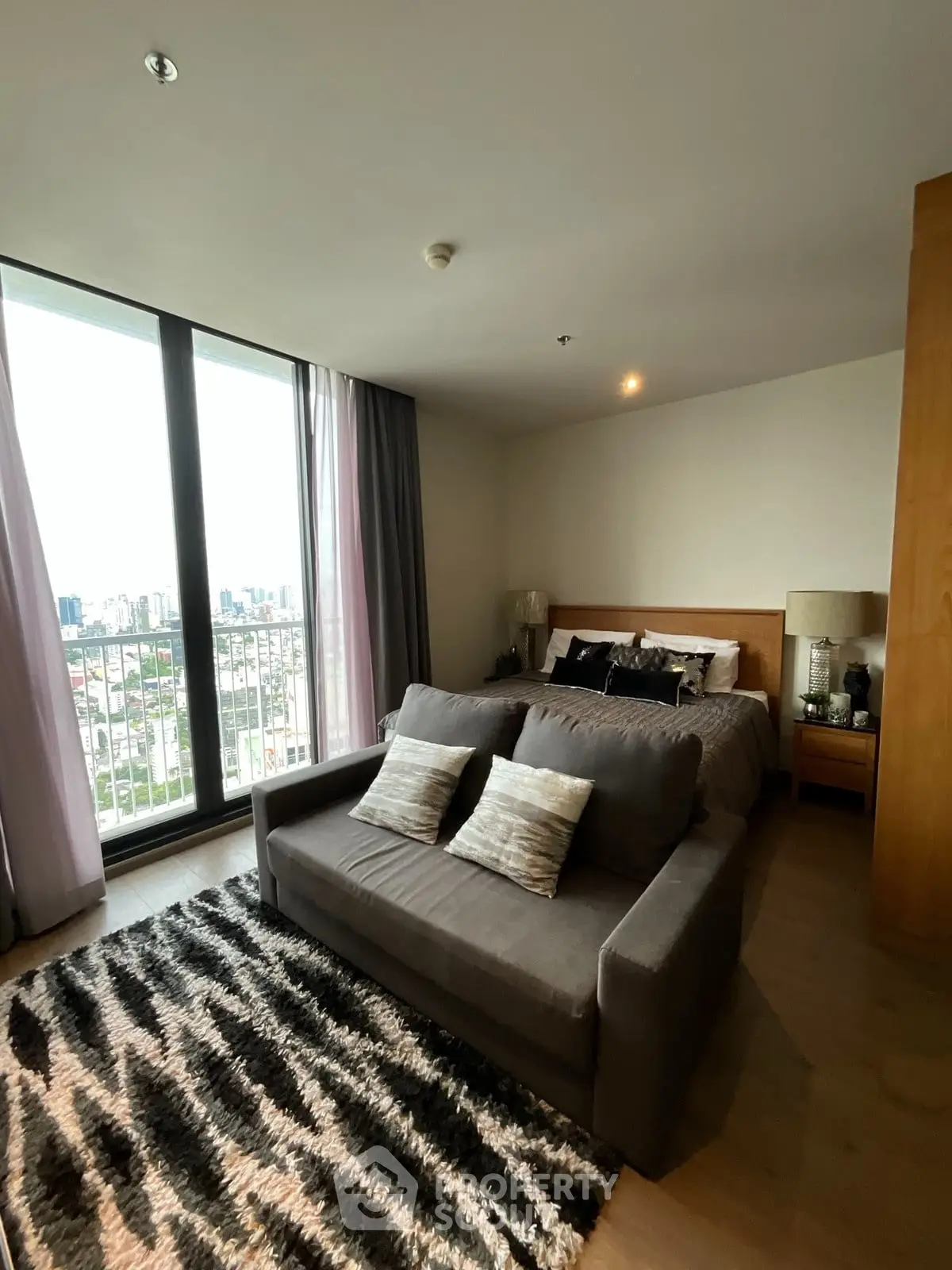 Stylish bedroom with city view, cozy sofa, and modern decor in high-rise apartment.