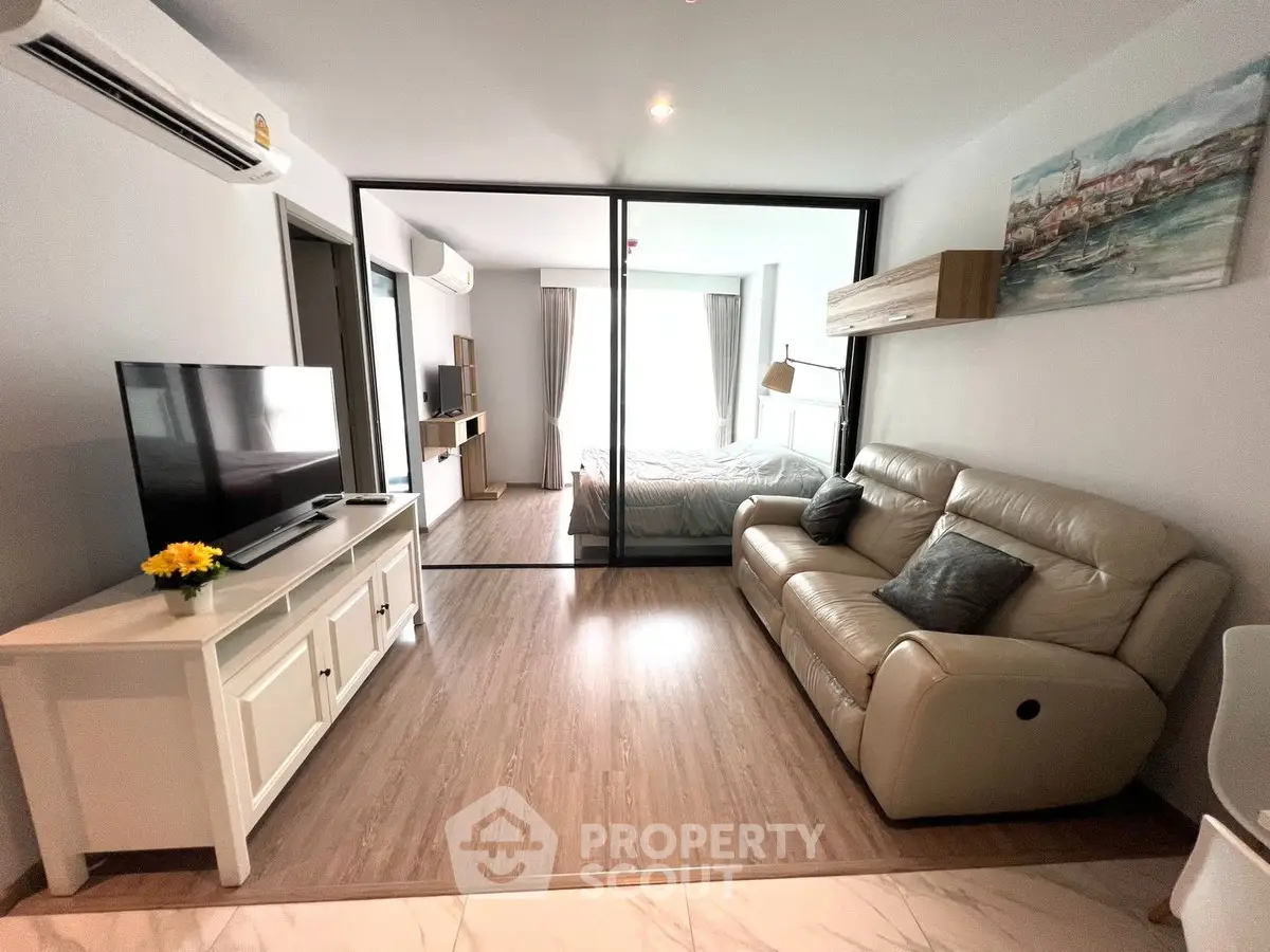 Modern living room with cozy leather sofa and large TV, open to a bright bedroom.