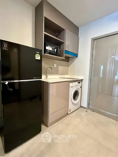Modern kitchen with sleek appliances including fridge, microwave, and washing machine in compact layout.