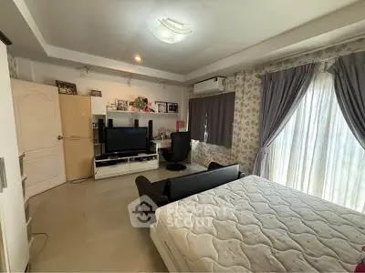 Spacious bedroom with modern decor and natural light, featuring a cozy seating area and entertainment setup.