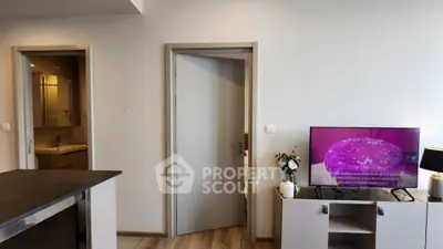 Modern apartment interior with open layout, featuring a TV on a stylish cabinet and a glimpse of a bathroom.