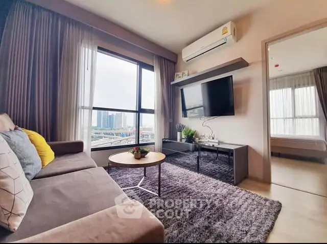 Modern living room with large windows and city view, featuring cozy sofa and wall-mounted TV.
