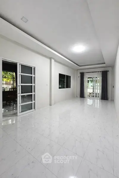 Spacious modern living room with large windows and sleek white flooring, perfect for natural light and open space.