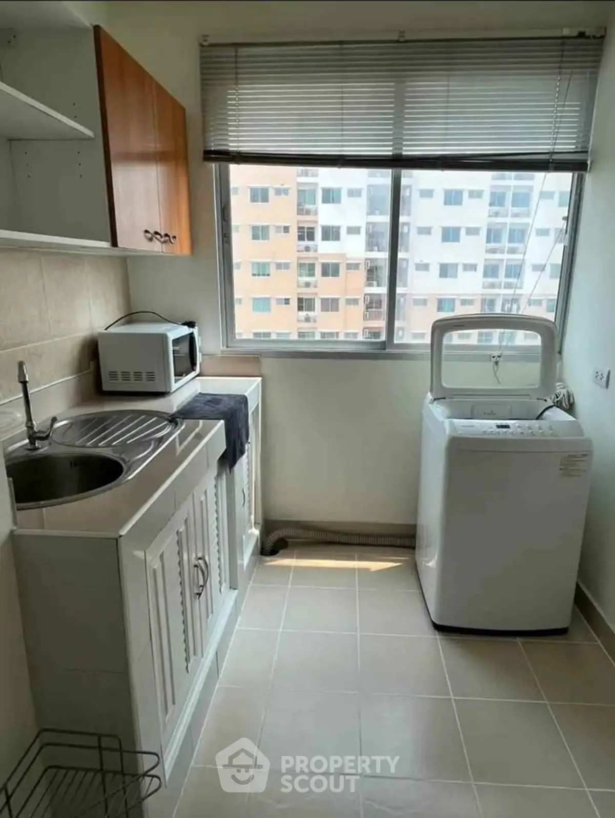 Compact kitchen with washing machine and microwave, featuring a large window with city view.
