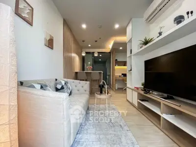Modern living room with stylish decor and open kitchen layout, featuring a cozy sofa and large TV.
