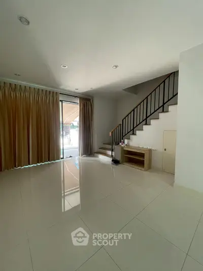 Spacious modern living room with large windows and elegant staircase