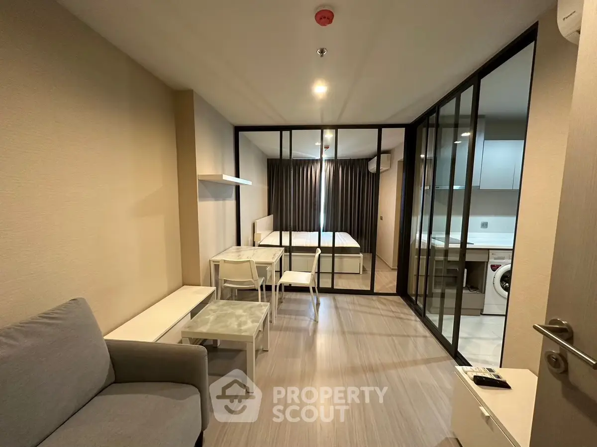 Modern studio apartment with glass partition, cozy living area, and compact kitchen.