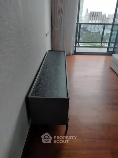 Spacious modern living room with wooden flooring and large windows offering city views.