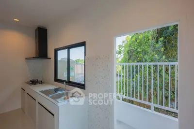 Modern kitchen with open layout and balcony view, featuring sleek countertops and gas stove.