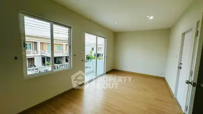 Spacious empty room with wooden flooring and balcony access in modern home