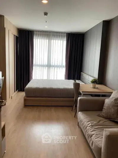 Modern studio apartment with cozy bed, sofa, and dining area, featuring elegant wooden flooring and large window.