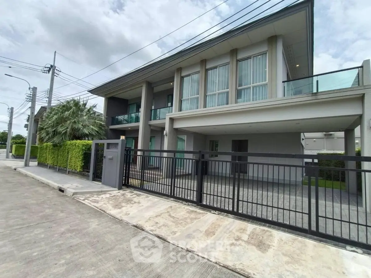 Modern two-story house with large windows and gated entrance in a suburban neighborhood.