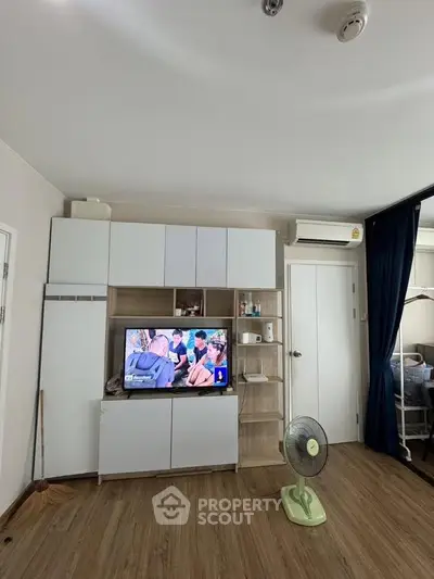 Modern living room with sleek entertainment unit and wooden flooring, featuring a TV and air conditioning.
