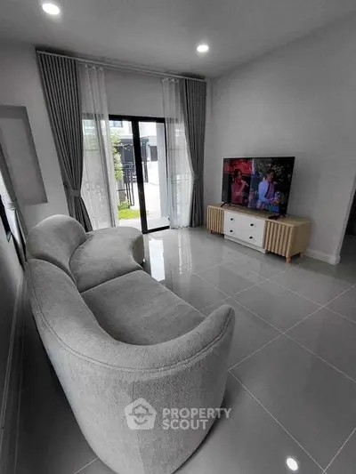 Modern living room with sleek gray sofa and large TV, featuring floor-to-ceiling windows and elegant curtains.