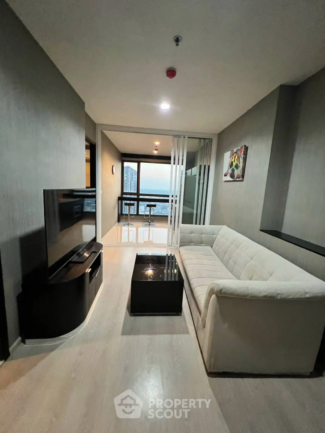 Modern living room with sleek design and city view, featuring a cozy sofa and flat-screen TV.