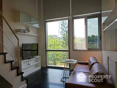 Bright and airy living room with high ceilings, large windows offering a lush green view, and a cozy brown leather couch, complemented by a sleek staircase.