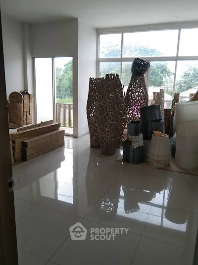 Spacious room with large windows and wicker decor, offering a serene view of greenery.