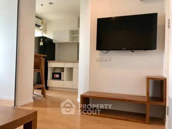 Modern apartment interior with wall-mounted TV and sleek kitchen area.