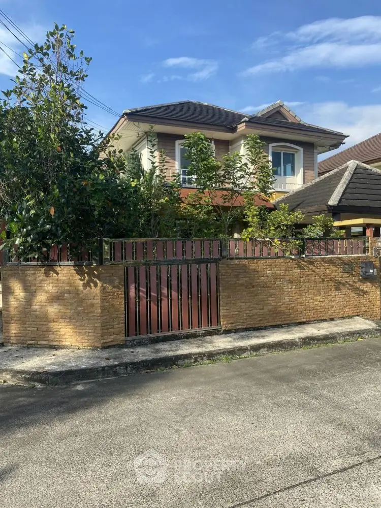 Charming two-story house with lush garden and brick fence in a serene neighborhood.