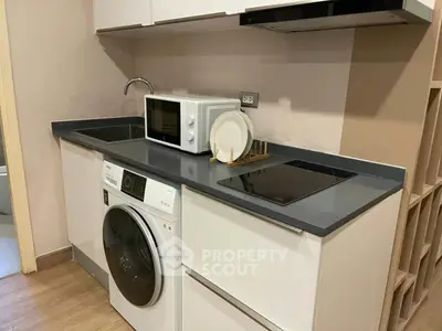 Modern compact kitchen with washing machine and microwave in sleek apartment.