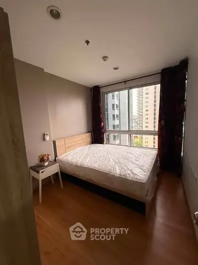 Cozy bedroom with large window offering city view, wooden flooring, and modern furnishings.