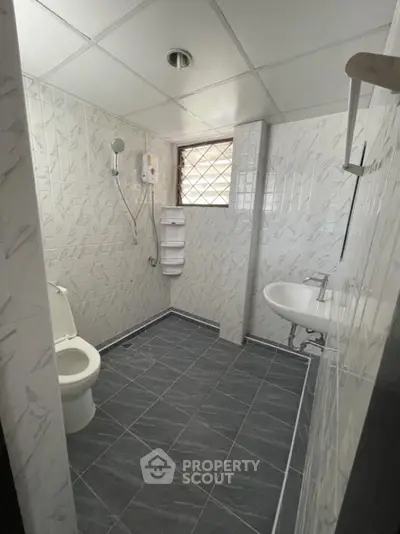Modern bathroom with tiled walls and floor, featuring a shower and white fixtures.