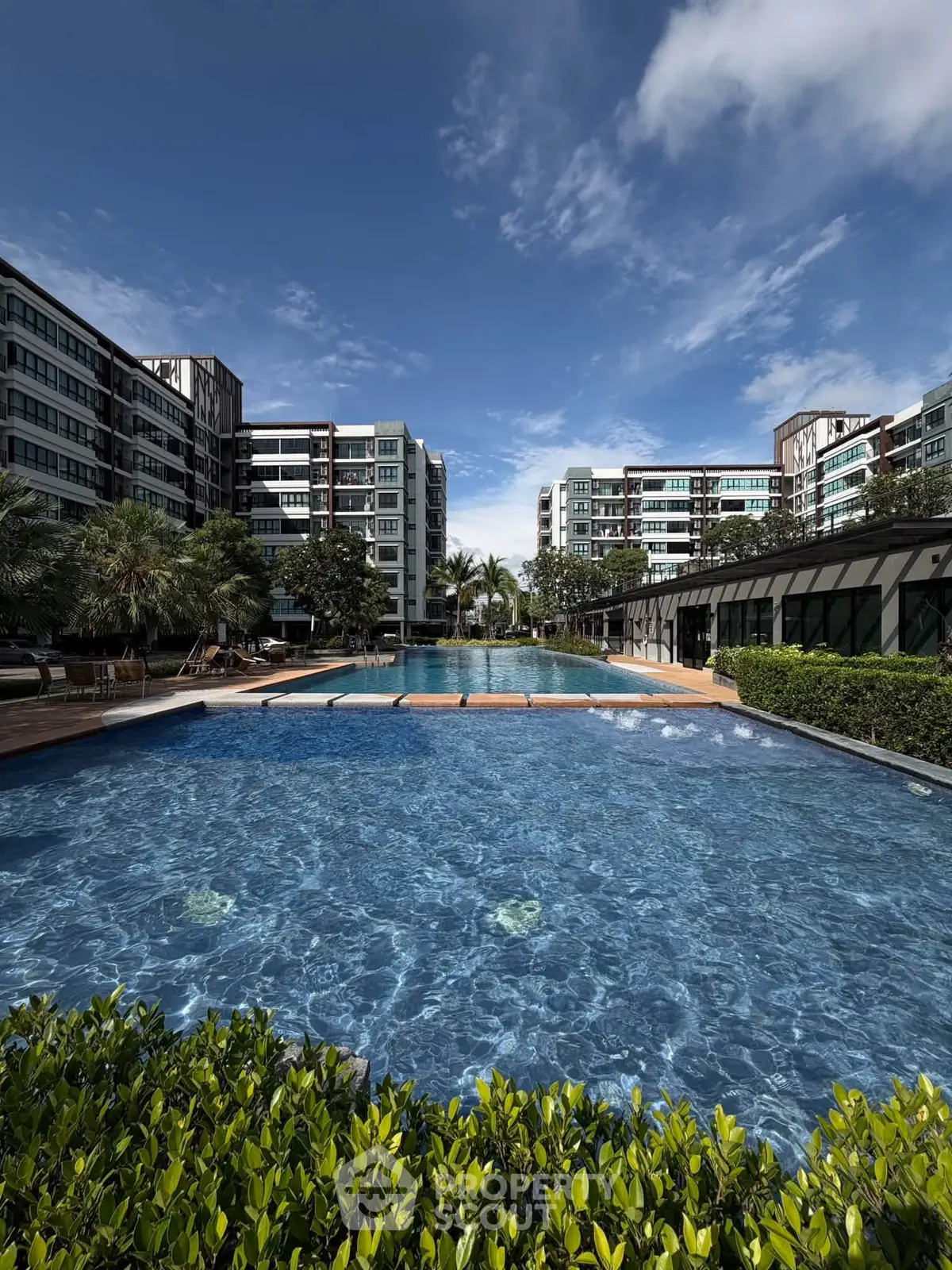 Luxurious residential complex with a stunning outdoor pool and modern architecture under a clear blue sky.