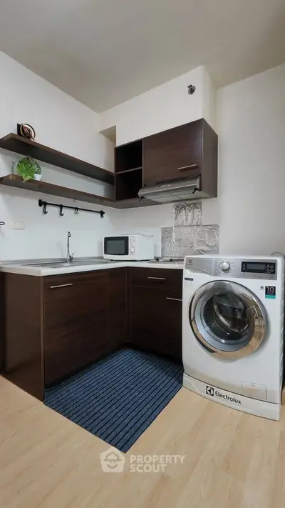 Modern kitchen with dark wood cabinets, washing machine, and microwave, perfect for compact living spaces.
