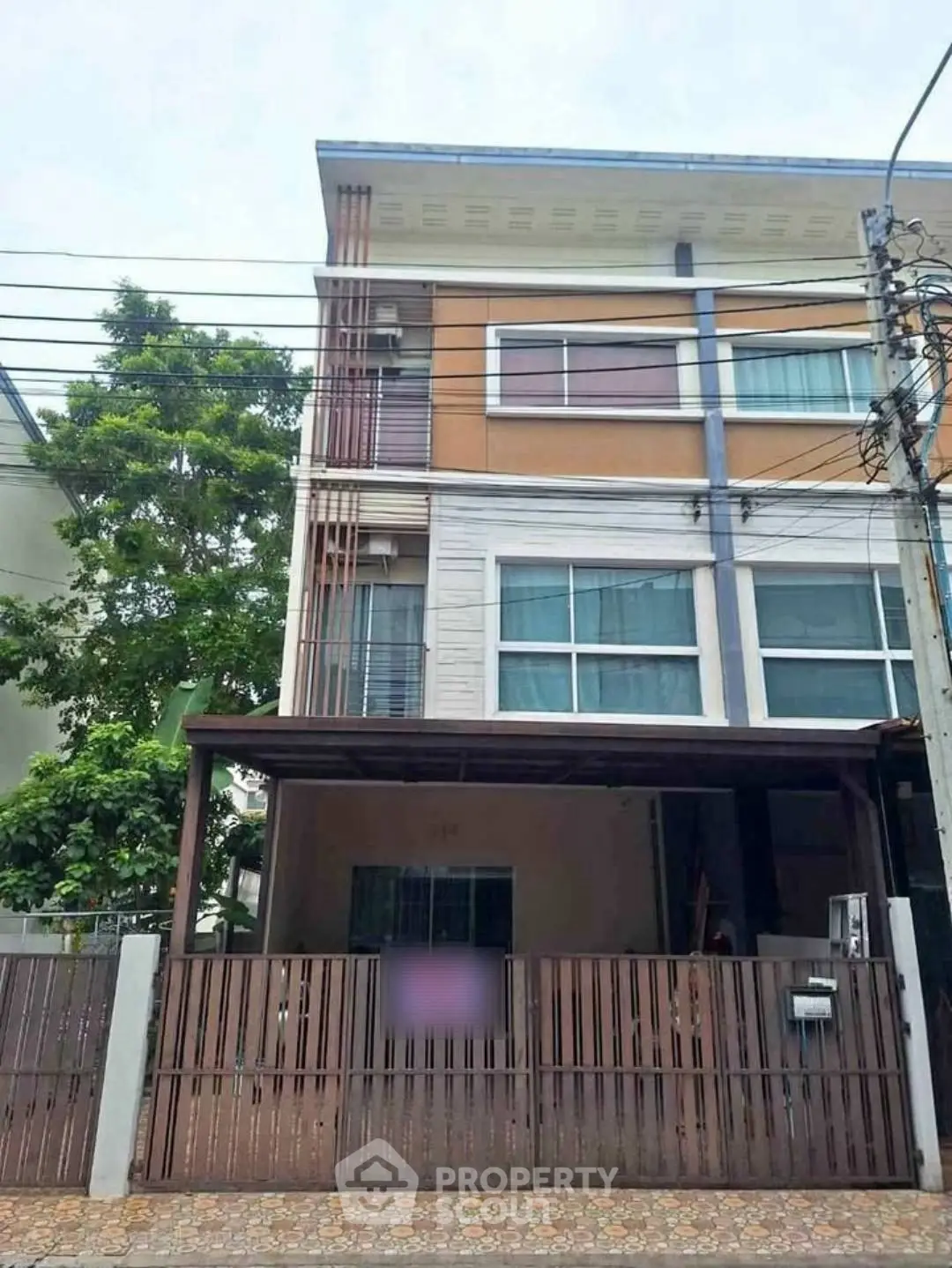 Modern three-story townhouse with gated entrance and carport in a suburban neighborhood.