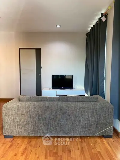Cozy living room with modern sofa and TV, featuring elegant curtains and wooden flooring.