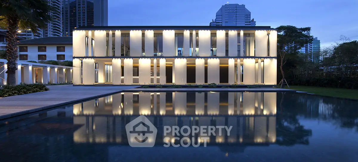 Luxurious modern building with stunning pool reflection at dusk, surrounded by lush greenery and cityscape.