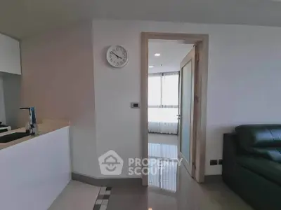 Modern apartment interior with sleek kitchen and cozy living area, featuring a wall clock and natural light.