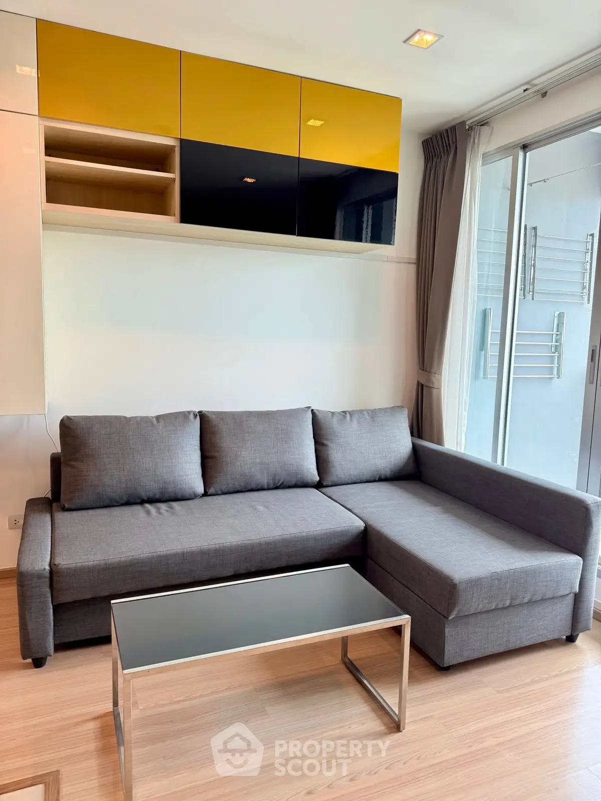 Modern living room with sleek gray sofa and glass coffee table, featuring stylish storage cabinets.