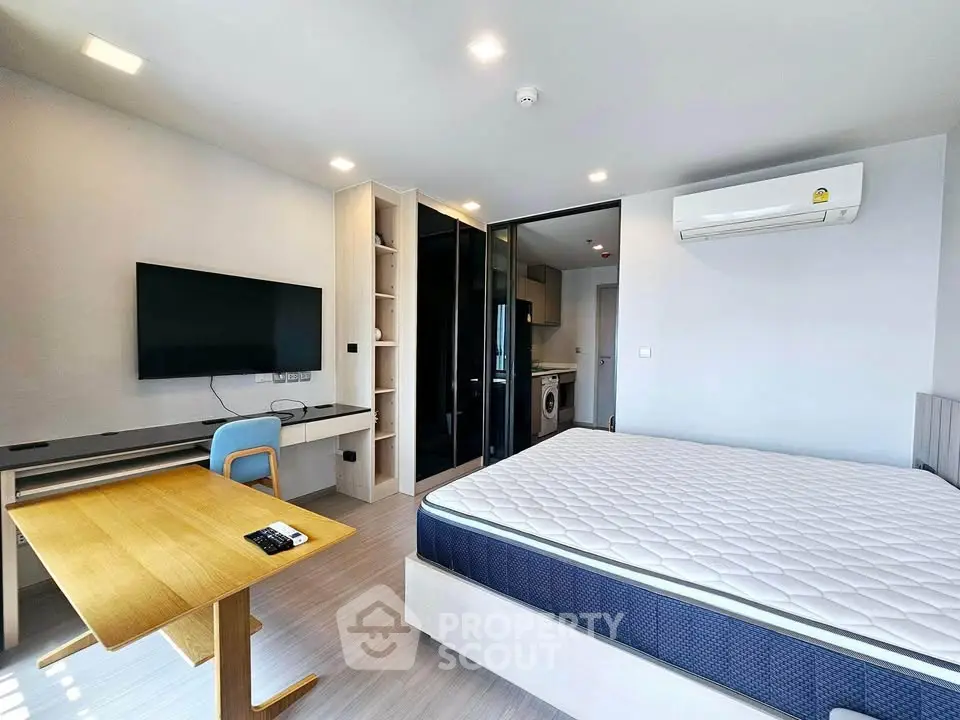 Modern studio apartment with sleek design, featuring a comfortable bed, wall-mounted TV, and compact dining area.