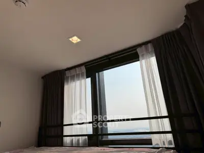 Cozy bedroom with large window offering a stunning city view, complemented by elegant curtains.