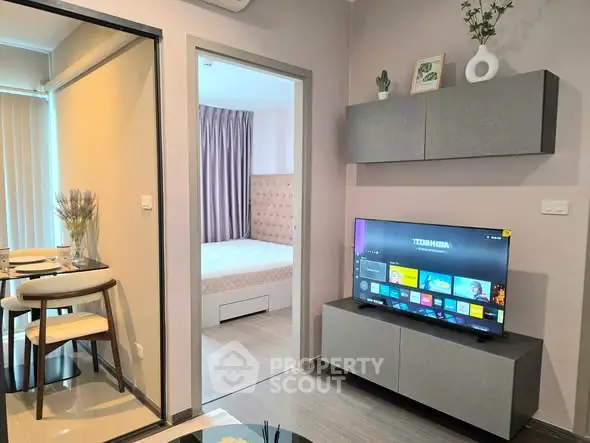 Modern living room with TV, stylish decor, and view into cozy bedroom in contemporary apartment.