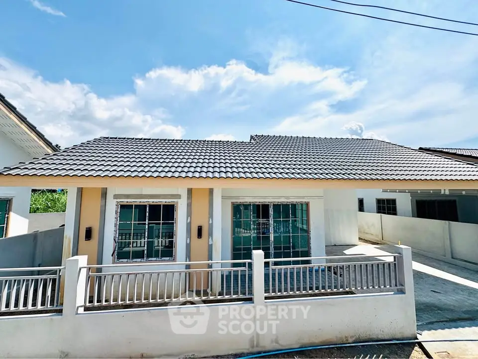 Charming single-story house with modern roof and fenced yard under a bright blue sky.