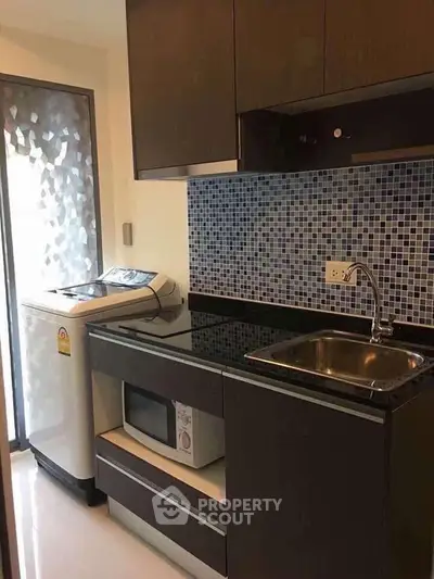 Modern kitchen with washing machine and microwave, featuring sleek cabinetry and mosaic backsplash.