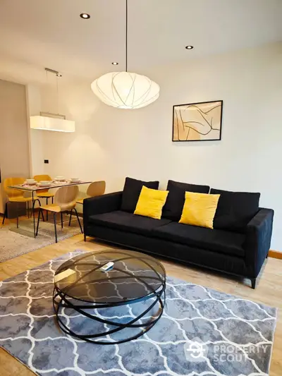 Chic modern living room seamlessly connected to a stylish dining area, featuring a plush black sofa with vibrant yellow cushions, an artistic glass coffee table, and elegant lighting fixtures.