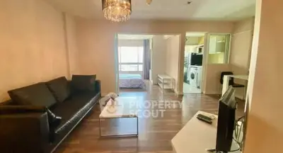 Spacious living room with modern decor and view into bedroom, featuring elegant chandelier and sleek furniture.