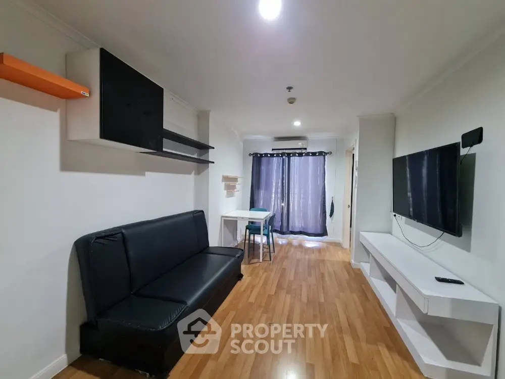 Modern living room with sleek black sofa and wall-mounted TV, featuring stylish wooden flooring.