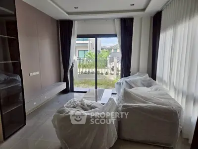 Modern living room with large windows and covered furniture, offering a view of the garden.