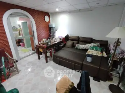 Spacious living room with a cozy brown sectional sofa, brick accent wall, and an arched doorway leading to another room, perfect for family gatherings.