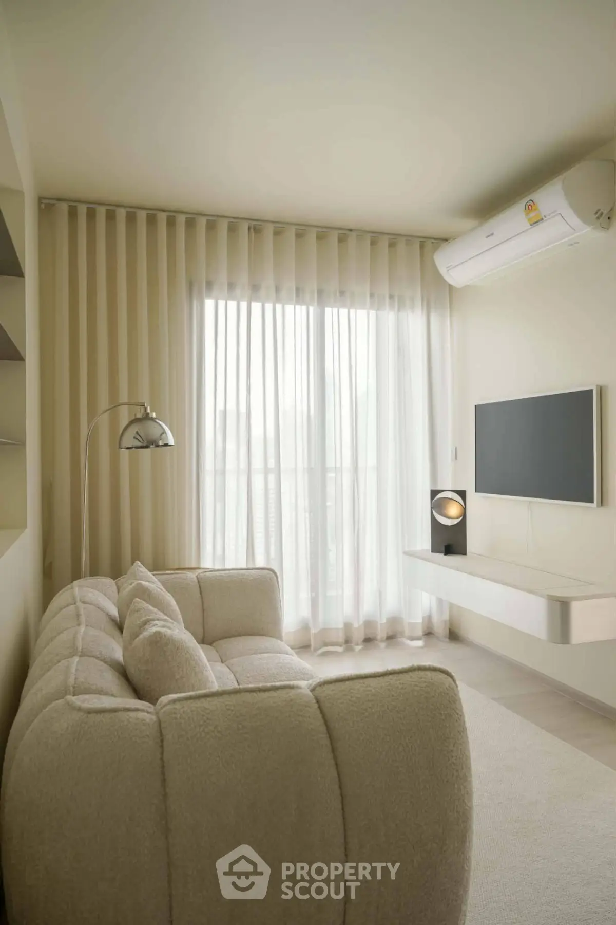 Modern living room with cozy sofa, wall-mounted TV, and large window with sheer curtains.