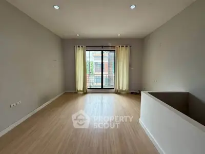 Spacious empty living room with wooden flooring and large window for natural light.