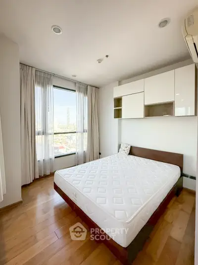 Bright and spacious bedroom with large window and modern furnishings in a high-rise apartment.